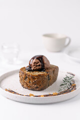 A slice of bread topped with chocolate ice cream and drizzled with chocolate sauce on a white plate, garnished with a sprig of rosemary.