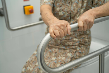 Asian elderly woman patient use toilet support rail in bathroom.