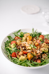 Fresh salad with quinoa, avocado, cherry tomatoes, roasted squash, arugula, and sliced almonds in a white bowl.