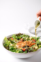 Fresh salad with grilled chicken, mixed greens, cherry tomatoes, and creamy dressing being poured from a small jug.