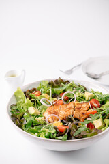 A fresh salad bowl with grilled chicken, avocado, cherry tomatoes, red onions, and mixed greens, accompanied by a small dressing pitcher.