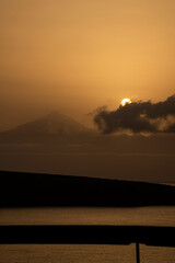 A mountain range is in the background with a large sun in the sky. The sky is a mix of orange and purple hues