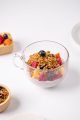 A glass cup filled with chia pudding topped with granola, blueberries, and assorted fresh fruits on...