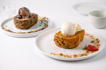 Two plated dessert servings featuring French toast topped with scoops of ice cream and garnished with strawberries and crumbs.