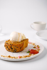 A slice of toasted bread topped with two scoops of vanilla ice cream, garnished with a strawberry and crumbs on a white plate.