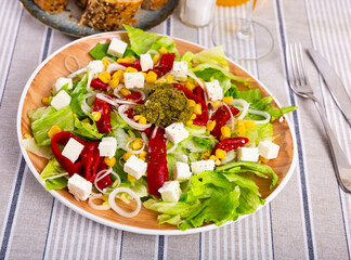 Delicious salad of fresh vegetables with corn, peppers, feta and pesto sauce on plate