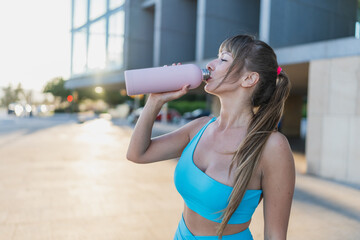 A woman drinking water from a bottle after her workout outdoors in the city, promoting hydration...