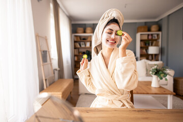 Smiling Woman in Soft Bathrobe and Head Towel Applying Natural Skincare Products in Sunlit Home Setting