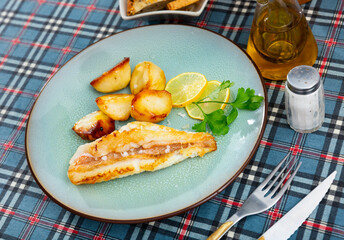 On plate, fried half carcass redfish garnished with boiled roasted potatoes. Dish for lunch in restaurant. Close-up. Grilled sea fish with side dish of potatoes.