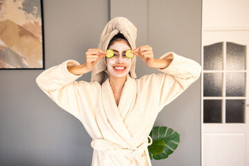 Cheerful Woman In Luxurious Cream Bathrobe With Hair Towel Enjoying Home Spa Treatment With Cucumber Slices