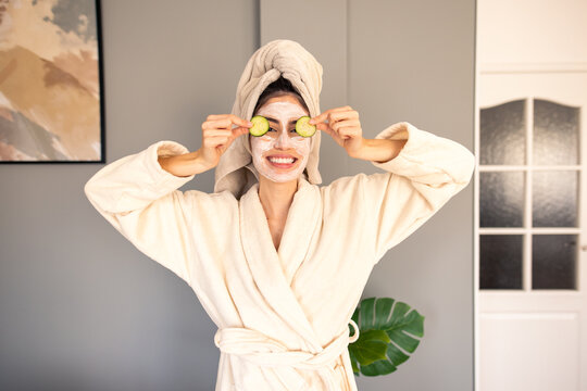 Cheerful Woman In Luxurious Cream Bathrobe With Hair Towel Enjoying Home Spa Treatment With Cucumber Slices