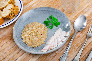 Appetizing oatmeal porridge served with lard on plate for breakfast