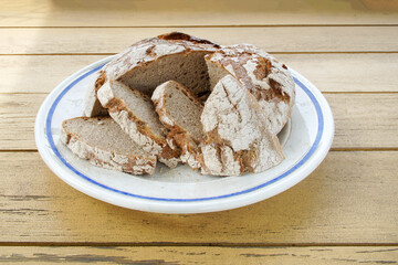 Rye bread, sprinkled with flour and cut into pieces, lies on the table on a large platter with a blue border.