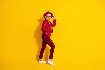 Fashionable elderly woman in bright red outfit posing playfully against solid yellow background showcasing vibrant style