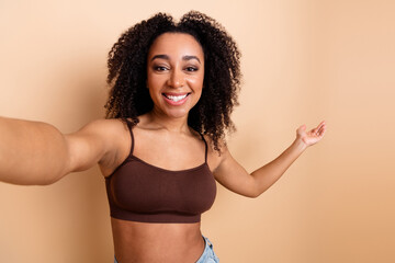 Portrait of a cheerful young woman with curly hair, posing against a beige background, wearing...