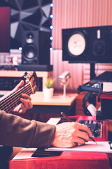 male musician hands writing a hit song by playing acoustic guitar and electric piano in home recording studio. songwriting, music education concept