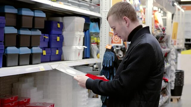 Construction worker selecting a red toolbox in a hardware store. Holding the toolbox, examining its features and determining its suitability for specific tasks. A man selects a toolbox