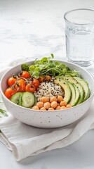 Healthy quinoa bowl with avocado and cherry tomatoes, paired with a glass of water. The white linen and wooden table set a bright, cozy dining scene.