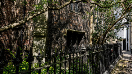 Sunlight filtering through leaves casts dancing shadows on an old brick building behind a wrought...