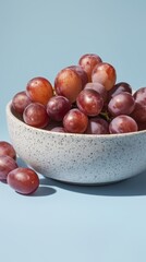 Cropped studio composition of red grapes in a speckled porcelain bowl set against a light blue backdrop. The minimalist styling and blank space offer room for text and highlight vibrant fruit color.