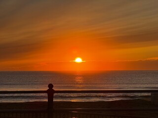 Fototapeta premium Golden sunrise over calm Atlantic waters at Virginia Beach with soft reflections and silhouetted railing