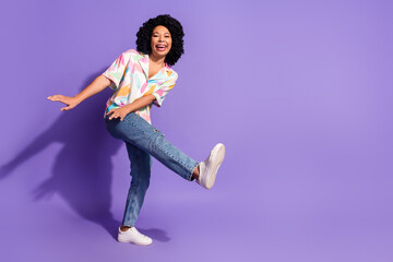 Cheerful young woman dancing playfully in trendy summer outfit with vibrant purple backdrop...