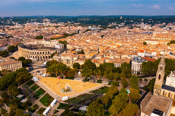 Naklejka premium Drone view of ancient Roman amphitheatre Arena of Nimes on background of reddish tiled roofs of residential buildings on summer day, France