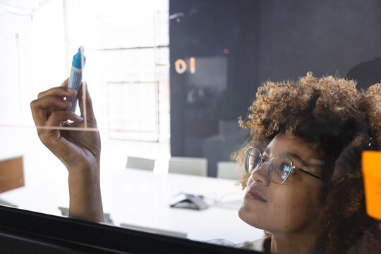 African American woman writing on whiteboard with blue marker near orange note in meeting room