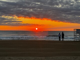 Couple stands by the shoreline at Virginia Beach watching the sunrise over calm waves