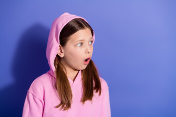 Surprised young girl in a pink hoodie looking off camera against a violet backdrop showcasing a fun...