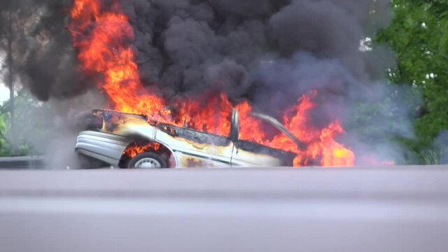 Car on road burning with large flames coming out.
