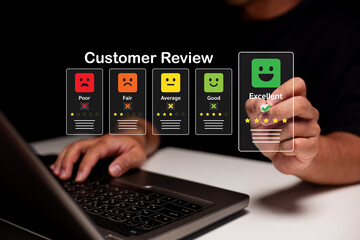 A person interacts with a digital customer review system, selecting an excellent rating with happy face icons above a laptop keyboard.
