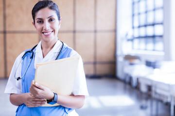 Hispanic nurse in scrubs holding folder and stethoscope checking wristwatch in corridor, copy space