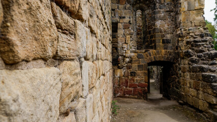 Weathered stone wall forms a passageway within the ruins of a historic castle, showcasing the aged textures and architectural details of the past