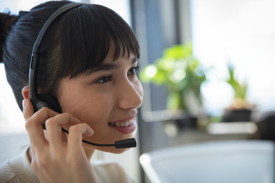 Female support representative smiling and holding headset at desk by window with plants, copy space