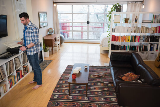 Man retrieving printed sheet from printer near vinyl shelves in studio apartment, copy space