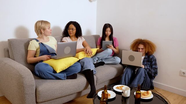 Multiethnic friends enjoy leisure time on a sofa, using laptops and a tablet, captured in slow motion