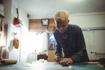 Female artisan cutting brown leather with rotary cutter at table in studio, copy space