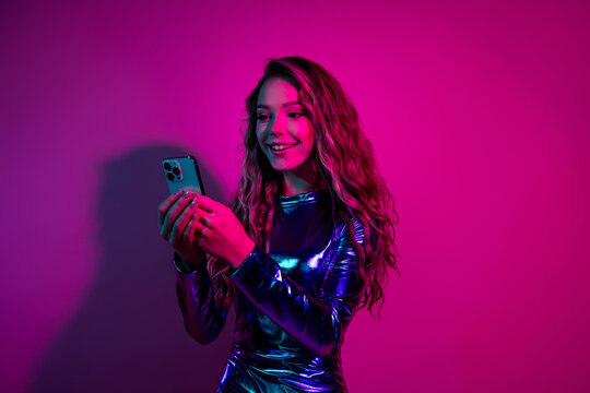 Smiling woman girl in shiny blue dress using smartphone against a vibrant pink background - Powered by Adobe