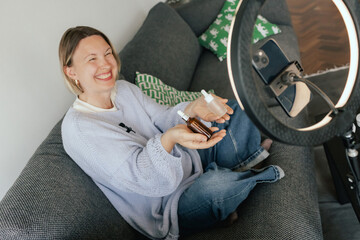 Middle-aged woman beauty blogger filming skincare product unboxing at home with ring light....