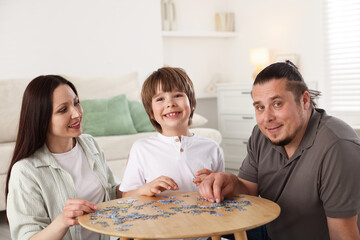 Parents with their son solving puzzle together at table indoors