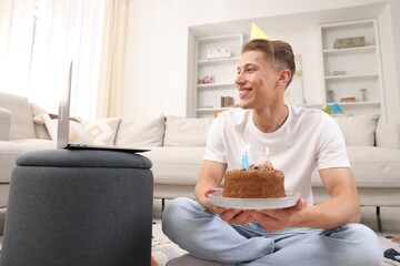 Man with cake celebrating his birthday and having video call via laptop at home