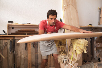 Male craftsman leaning over foam surfboard blank at shaping workshop using hand tools