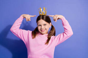 Smiling girl in pink hoodie posing confidently with golden crown against vibrant purple backdrop