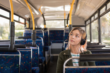 Woman sitting in public bus on patterned seats wearing over-ear headphones and jacket, copy space