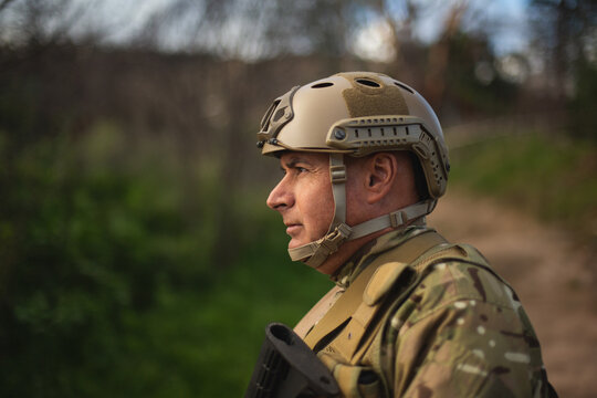 Mature male soldier standing on dirt track wearing tactical gear while holding rifle copy space