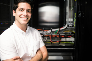 Man standing with arms crossed in server room beside server rack and network cables, copy space