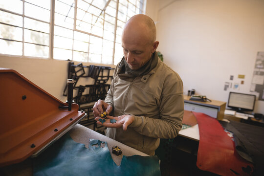 Middle-aged male craftsman punching teal and red leather hides with punch tool in leather workshop