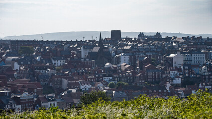 Panoramic view of Whitby in North Yorkshire, England, showcasing its historic buildings, rooftops, and the distant North York Moors National Park