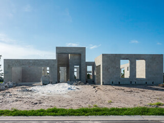 Street view of the concrete shell of a single-family house under construction, with a rectangular design, in a suburban residential development on a sunny evening in southwest Florida